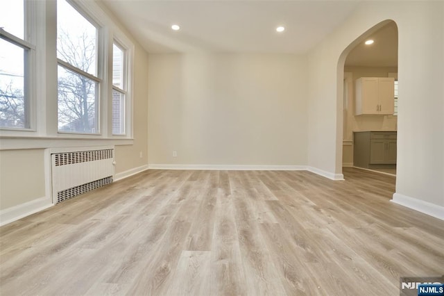 unfurnished room with radiator, light wood-type flooring, baseboards, and arched walkways