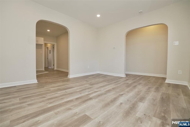 spare room with light wood-style floors, baseboards, and arched walkways