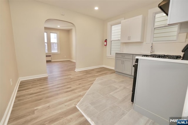 kitchen with arched walkways, recessed lighting, light wood-style floors, radiator, and gas range