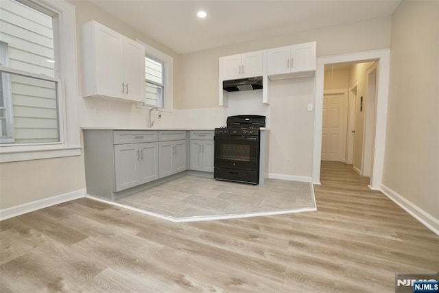 kitchen featuring light wood-style flooring, gas stove, under cabinet range hood, and baseboards