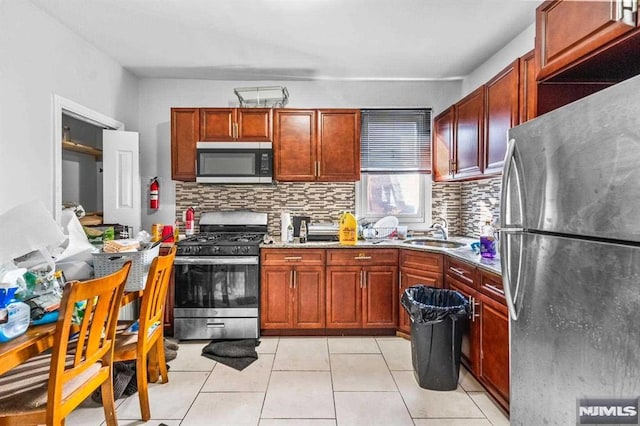 kitchen featuring light tile patterned flooring, a sink, appliances with stainless steel finishes, backsplash, and light stone countertops