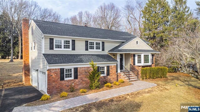 view of front of property featuring driveway, a chimney, roof with shingles, an attached garage, and brick siding