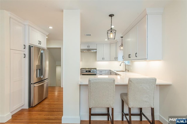 kitchen with a breakfast bar area, a peninsula, a sink, light wood-style floors, and appliances with stainless steel finishes