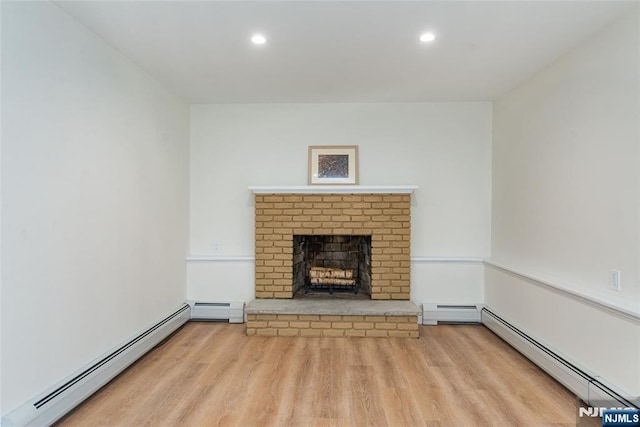 unfurnished living room with baseboard heating, a brick fireplace, and wood finished floors