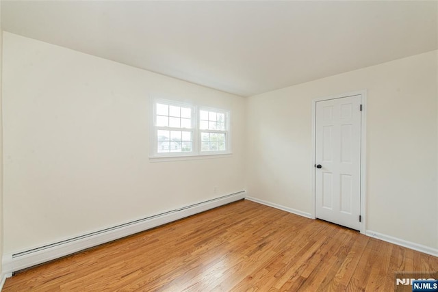 spare room featuring light wood finished floors, a baseboard radiator, and baseboards