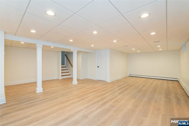 finished basement with light wood-style floors, baseboards, stairway, and a baseboard heating unit