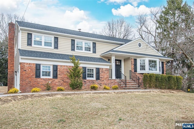 view of front of property featuring brick siding, a chimney, a shingled roof, and a front lawn