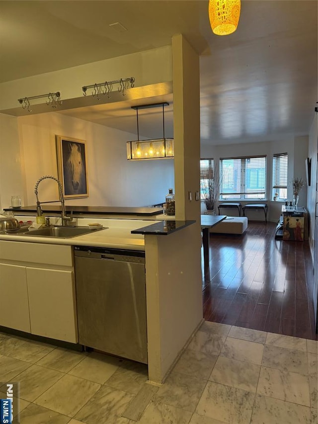 kitchen featuring pendant lighting, stainless steel dishwasher, open floor plan, white cabinets, and a sink