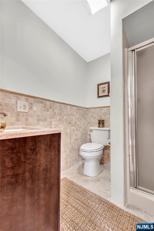 bathroom featuring toilet, a wainscoted wall, tile patterned flooring, vanity, and a shower stall