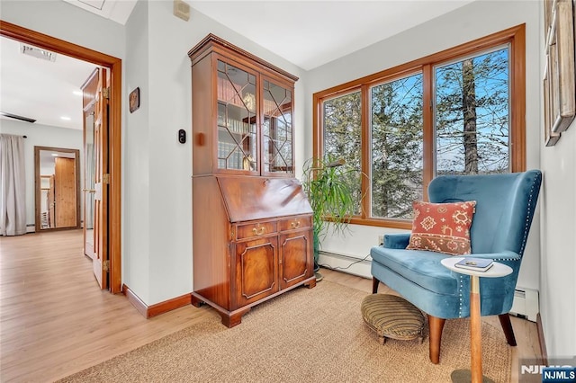 living area featuring a baseboard heating unit, light wood-style flooring, visible vents, and baseboards