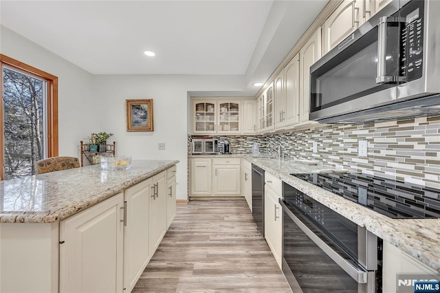 kitchen with glass insert cabinets, light stone countertops, appliances with stainless steel finishes, and light wood-style floors