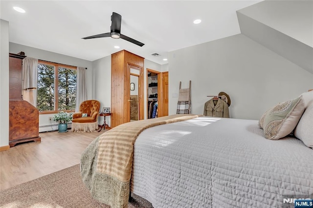 bedroom with a ceiling fan, wood finished floors, a walk in closet, a baseboard heating unit, and recessed lighting