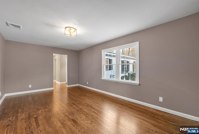 spare room featuring wood finished floors, visible vents, and baseboards