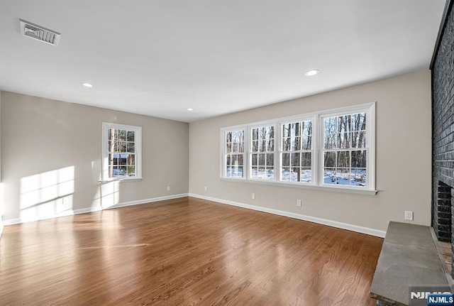 unfurnished living room with a brick fireplace, visible vents, baseboards, and wood finished floors