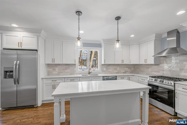 kitchen featuring decorative light fixtures, appliances with stainless steel finishes, white cabinetry, a sink, and wall chimney exhaust hood