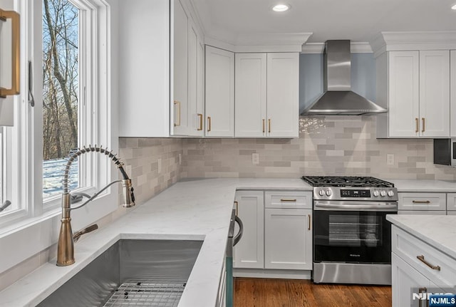 kitchen featuring stainless steel gas stove, wall chimney range hood, white cabinets, and a sink