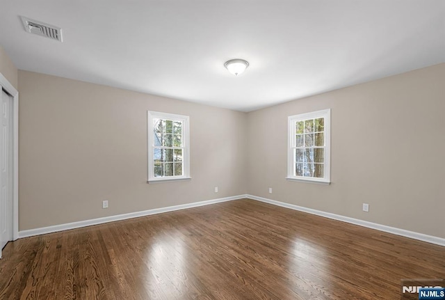 empty room with a wealth of natural light, dark wood-style flooring, visible vents, and baseboards