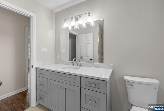 bathroom with toilet, wood finished floors, vanity, and baseboards