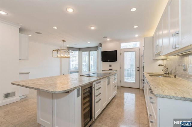 kitchen with beverage cooler, visible vents, a center island, hanging light fixtures, and white cabinetry