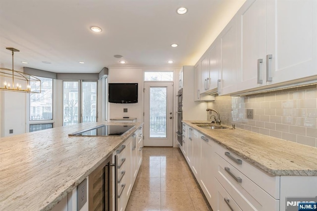 kitchen featuring white cabinets, light stone counters, black electric cooktop, and a sink