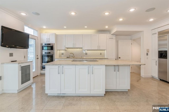 kitchen with decorative backsplash, appliances with stainless steel finishes, white cabinetry, an island with sink, and light stone countertops