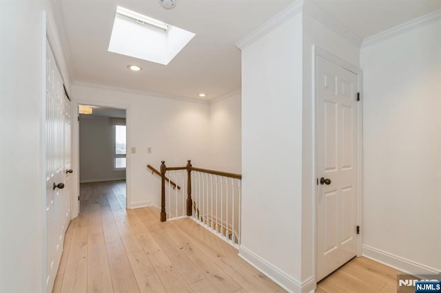 hallway with light wood finished floors, a skylight, and ornamental molding