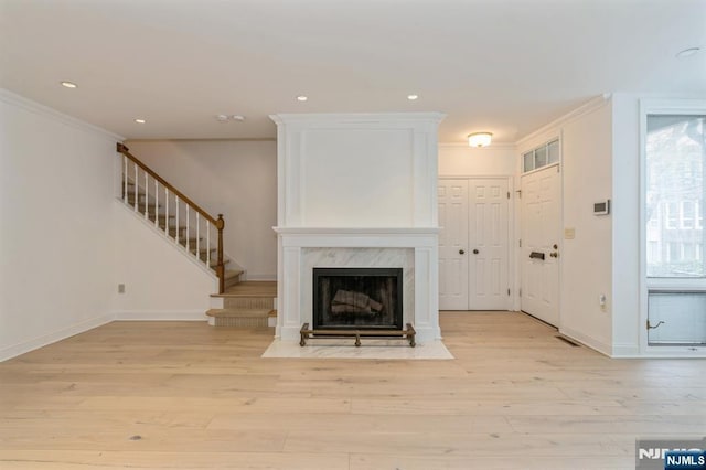 unfurnished living room featuring stairs, light wood finished floors, visible vents, and crown molding