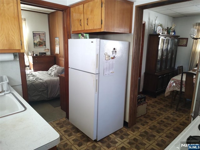 kitchen featuring brown cabinets, freestanding refrigerator, light countertops, a paneled ceiling, and a sink