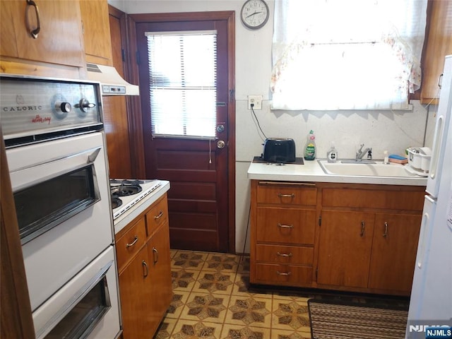 kitchen with brown cabinets, white appliances, light countertops, and a sink