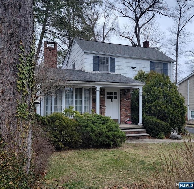 view of front of home with a front yard, a porch, and a chimney