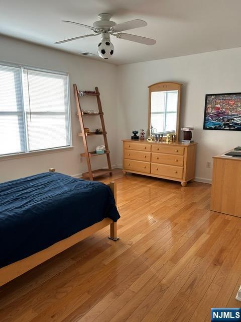 bedroom featuring light wood finished floors, ceiling fan, multiple windows, and baseboards