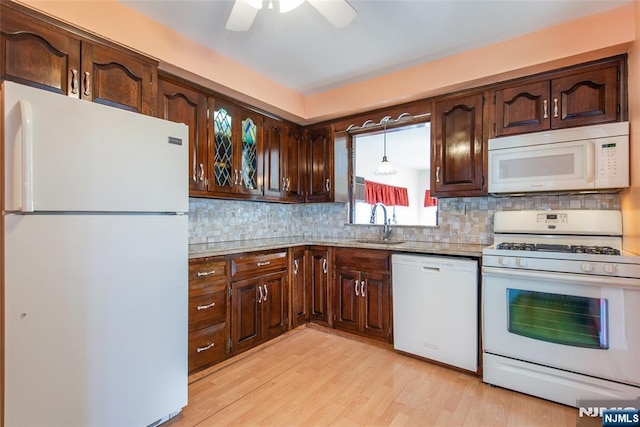 kitchen with white appliances, tasteful backsplash, light wood-style flooring, hanging light fixtures, and a sink