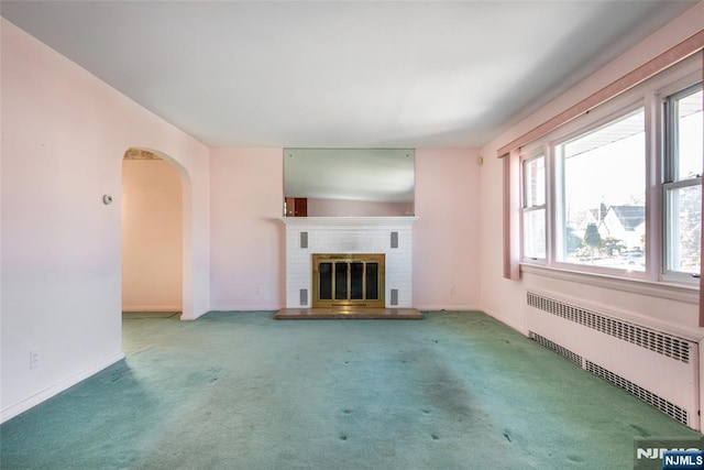 unfurnished living room featuring a brick fireplace, arched walkways, carpet, and radiator heating unit