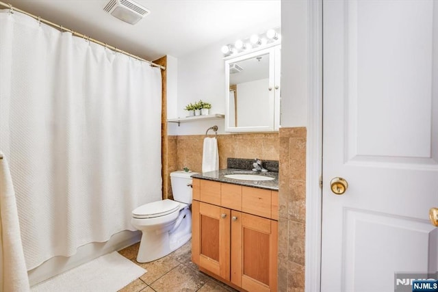 bathroom featuring tile patterned flooring, visible vents, toilet, vanity, and tile walls