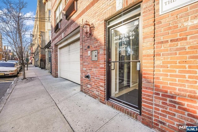 entrance to property with brick siding, driveway, and a garage