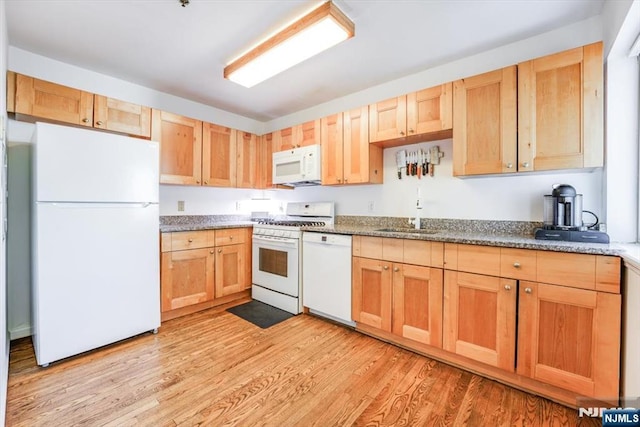 kitchen with light brown cabinets, light wood-type flooring, dark stone countertops, white appliances, and a sink