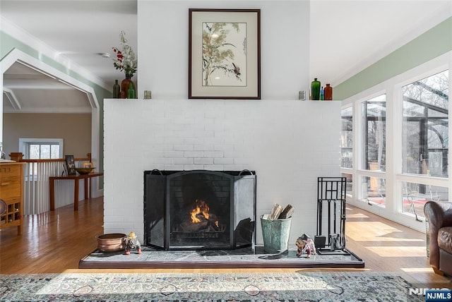 interior details with crown molding, arched walkways, a fireplace, and wood finished floors