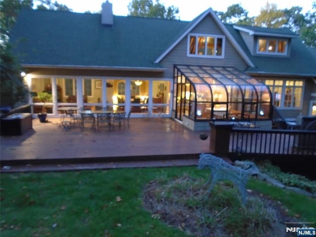 rear view of house with a chimney, a wooden deck, and a sunroom