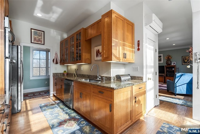 kitchen with a wall unit AC, light wood-style flooring, a sink, stainless steel dishwasher, and dark stone counters