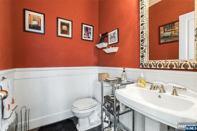 half bathroom with a wainscoted wall, a sink, and toilet