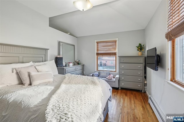 bedroom with a baseboard heating unit, vaulted ceiling, wood finished floors, and baseboards