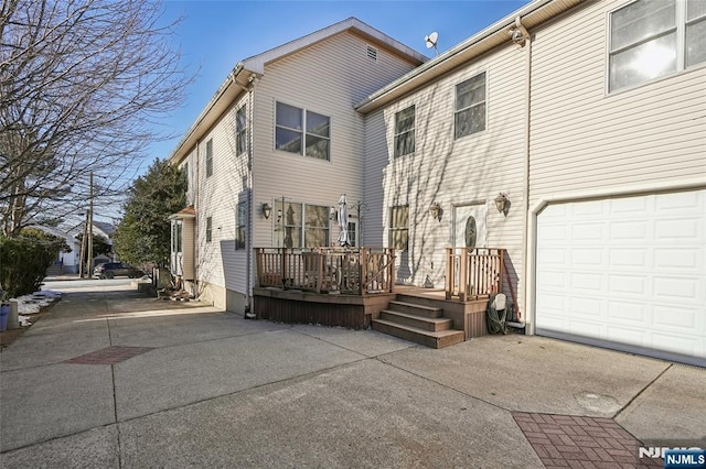 rear view of property with an attached garage, a deck, and concrete driveway