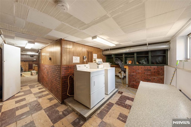 laundry room with brick wall, light floors, washing machine and dryer, and wooden walls