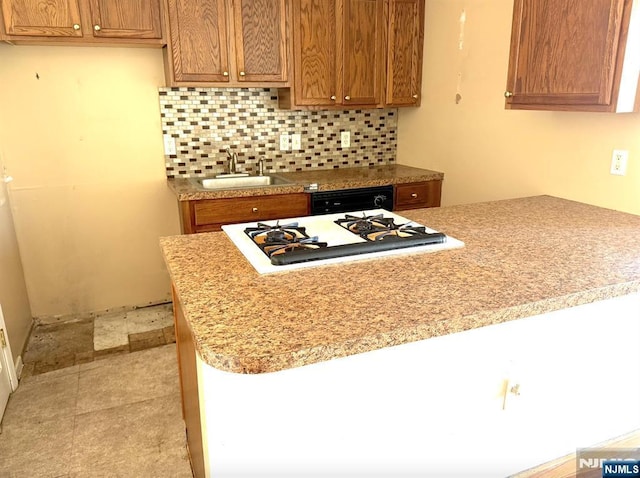 kitchen with brown cabinets, tasteful backsplash, light countertops, and a sink