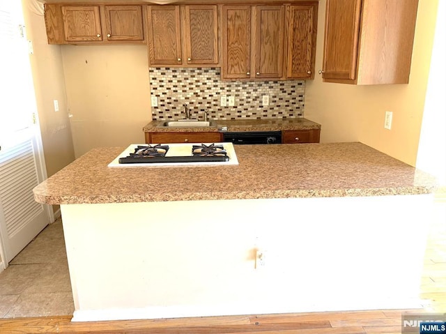 kitchen with a sink, tasteful backsplash, brown cabinetry, and gas stovetop