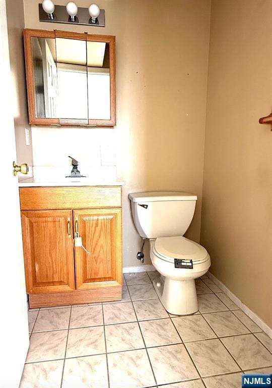 half bath featuring toilet, tile patterned flooring, vanity, and baseboards