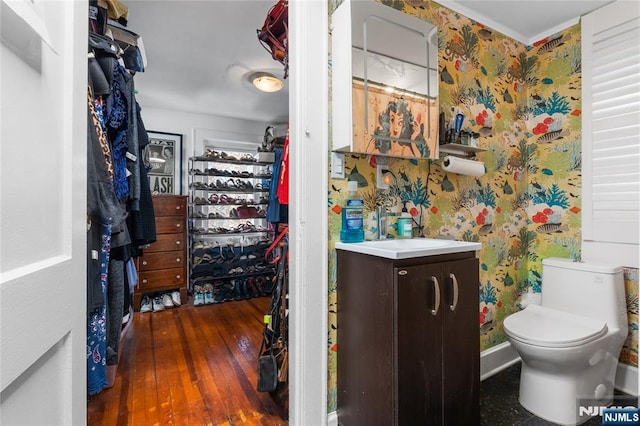 bathroom featuring toilet, wallpapered walls, wood finished floors, and vanity