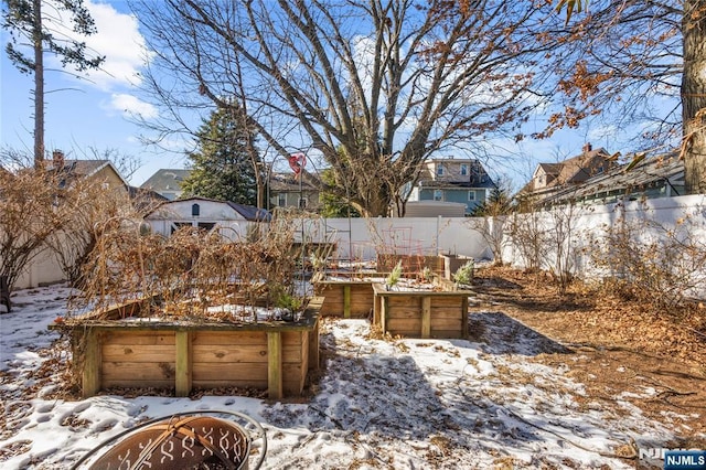 snowy yard featuring a garage, a fenced backyard, and a vegetable garden