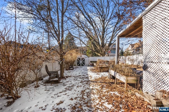 yard layered in snow with a storage unit, an outdoor structure, fence, and a garden