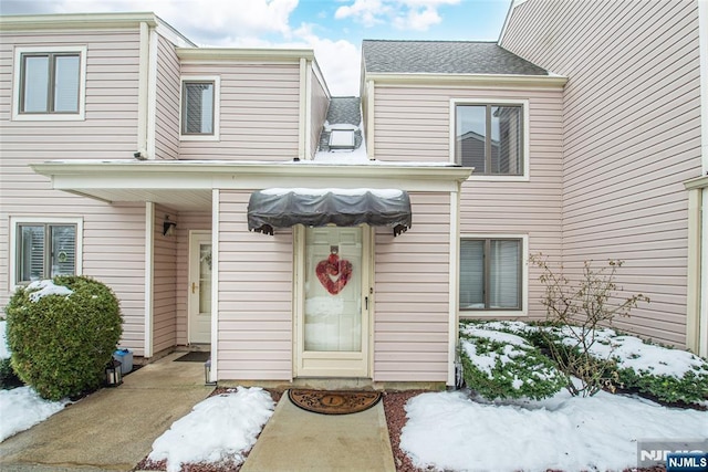 snow covered property entrance with roof with shingles